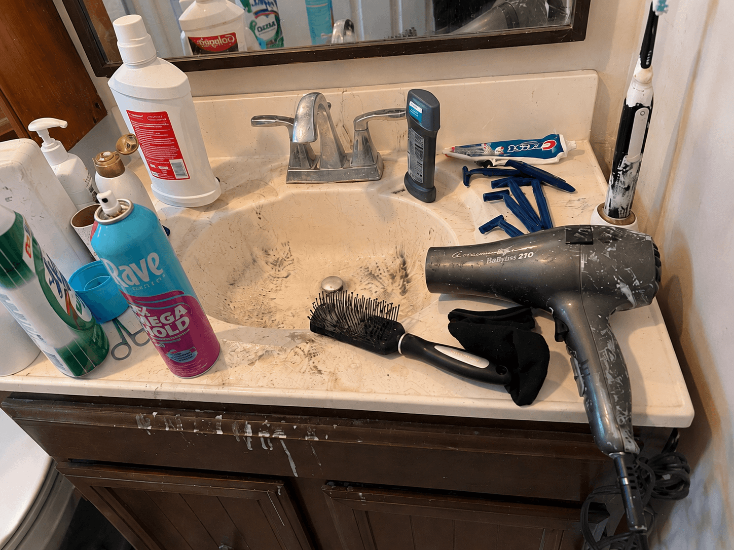 Bathroom sink crowded with toiletries and soiled around the basin before a ShinySpaces cleaning